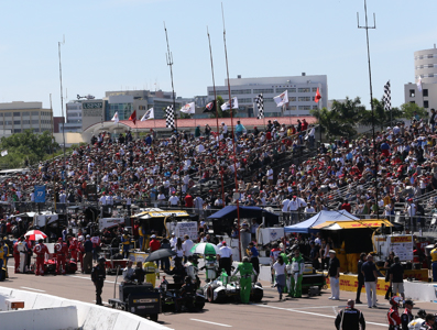 A large outdoor audience beside the track with some covered sections on the road side.