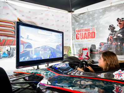 Someone in a mock racing car using a screen race simulator, with branding on the partition beside.